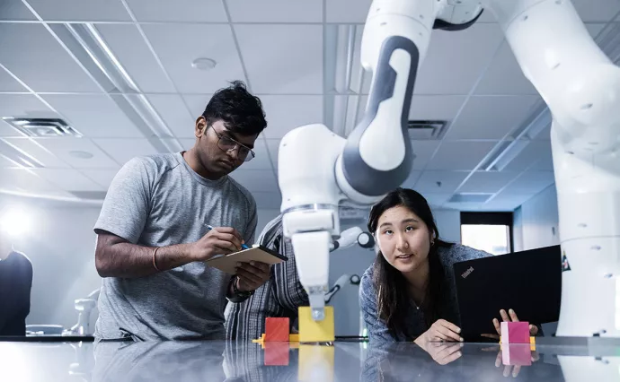 Two students study a robot and make observations
